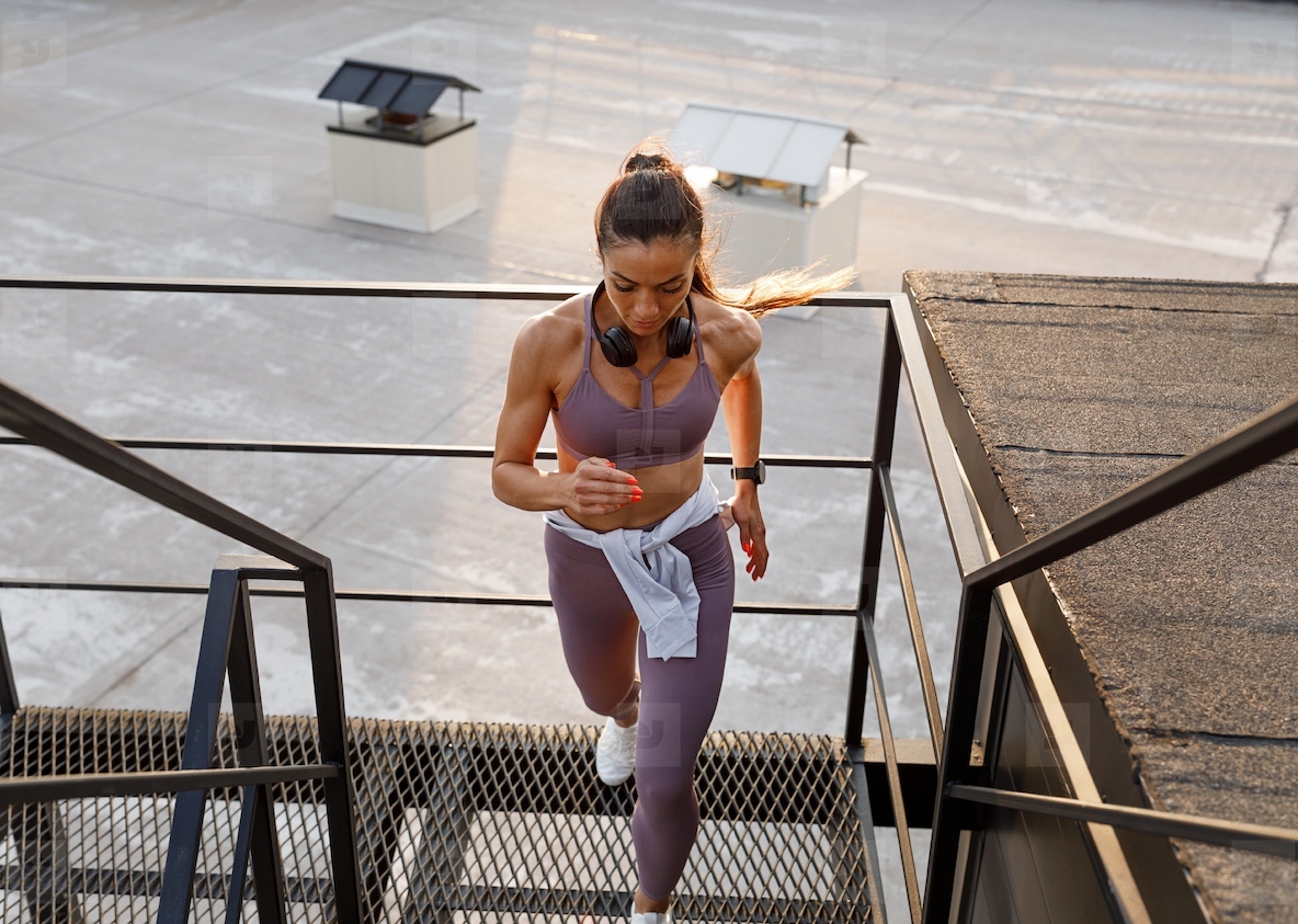 Full length of a muscular female runner on the stairs on the roof Woman in fitness attire running on the roof stairs