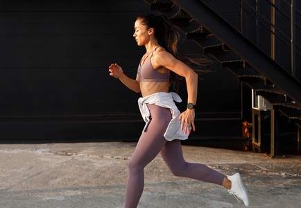 Side view of young female running at sunset in an urban environment  Muscular runner in sportswear sprinting outdoors