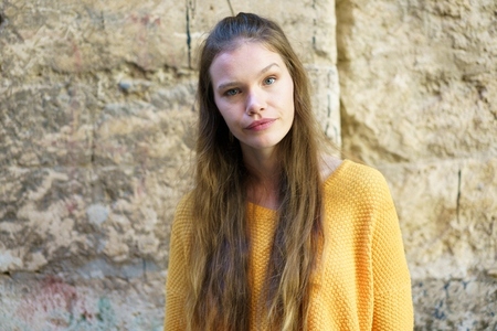 A Young Woman Dressed in a Bright Yellow Sweater Posing Elegantly Against a Stone Wall