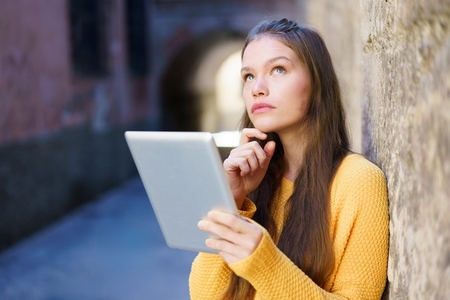 A Thoughtful Young Woman Deeply Engaged with Her Tablet amidst a Vibrant Urban Environment