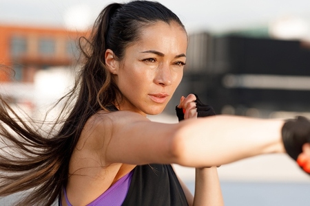 Young female practicing shadow boxing outdoors  Sportswoman with long hair warming up outdoors