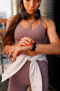 Cropped shot of young slim female wearing fitness wear and checking her smartwatch during an outdoor workout