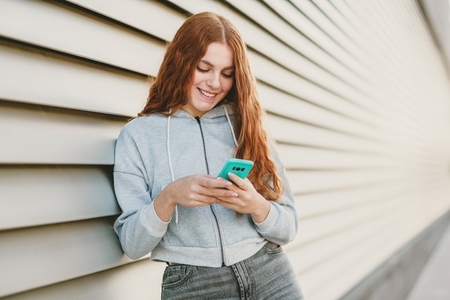 A young woman is texting on her smartphone while standing against a vibrant modern background A young woman is texting on her smartphone while standing against a vibrant modern background