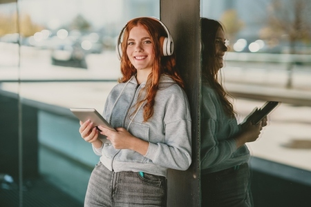 A young woman is enjoying her music while wearing headphones in a lively urban setting