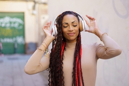 A Young Woman is Enjoying Listening to Music with Headphones in an Urban City Setting A Young Woman is Enjoying Listening to Music with Headphones in an Urban City Setting