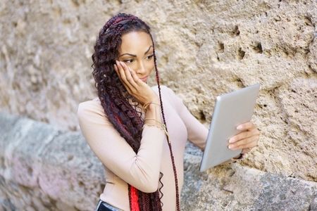 A woman is engaged with her tablet as she sits against a stone wall enjoying the moment A woman is engaged with her tablet as she sits against a stone wall enjoying the moment