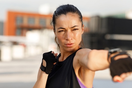 High detail outdoor portrait of a strong female in gloves practicing shadow boxing
