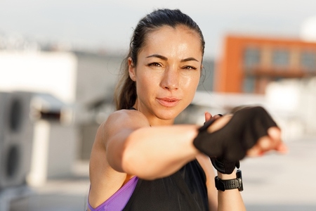 Young woman wearing gloves practicing shadow boxing outdoors  Portrait of a sportswoman looking at camera warming up