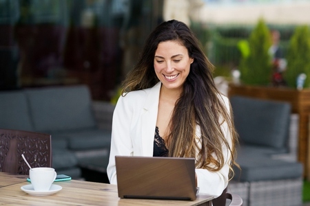 Professional Woman Smiling While Working on Laptop at Outdoor Caf
