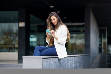 A young woman is using her smartphone outdoors while surrounded by a modern urban environment A young woman is using her smartphone outdoors while surrounded by a modern urban environment