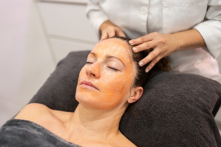 Beautician massaging head of woman with facial mask in beauty salon