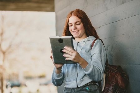 A joyful teenage girl is savoring engaging digital content on her tablet while outdoors A joyful teenage girl is savoring engaging digital content on her tablet while outdoors