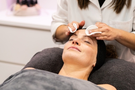 Crop beautician removing facial product from face with cotton pads