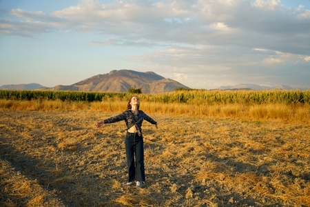 Embracing Nature Young Woman Standing in Open Field Surrounded by Majestic Mountains in Background