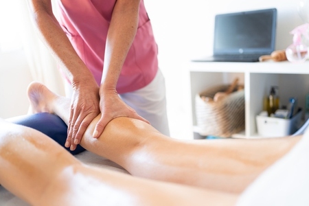 Crop masseuse putting pressure on leg of female client during body massage