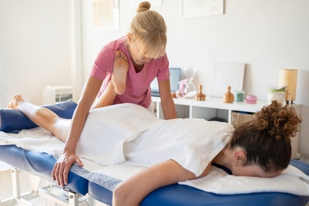 Serious masseuse doing massage on leg of female client
