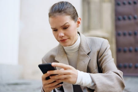 A young woman is sitting outside in an urban setting  engaged with her smartphone device