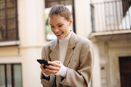 A Charming Smiling Woman Engaged in Texting on Her Smartphone While in an Urban Setting A Charming Smiling Woman Engaged in Texting on Her Smartphone While in an Urban Setting