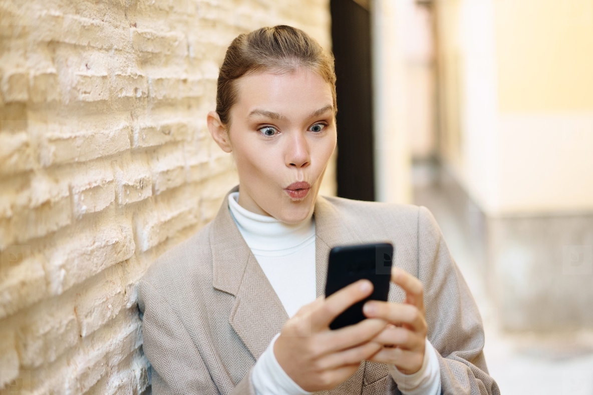 A surprised woman is engaged with her smartphone while sitting in a modern and vibrant setting