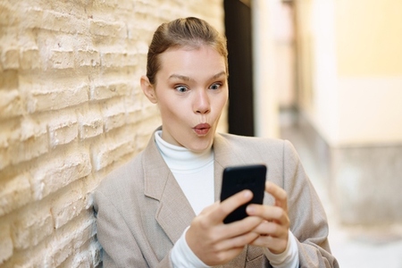 A surprised woman is engaged with her smartphone while sitting in a modern and vibrant setting A surprised woman is engaged with her smartphone while sitting in a modern and vibrant setting