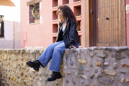 A young woman sits on a stone wall in a trendy outfit showcasing her style and confidence A young woman sits on a stone wall in a trendy outfit showcasing her style and confidence