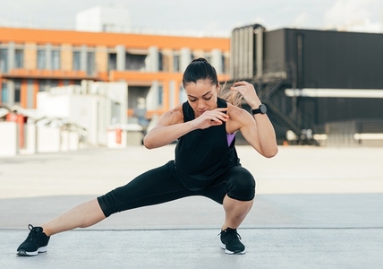 Young female doing warming up exercises on the roof  Woman in sportswear warming up her legs