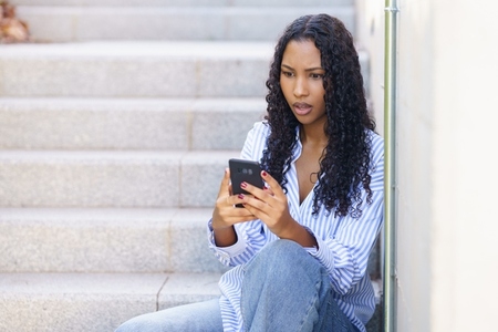 A young woman is deeply engrossed in her mobile phone while comfortably sitting on some steps