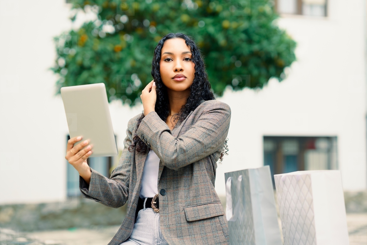 A Stylish Young Woman Engaging Enthusiastically with a Tablet Amidst Shopping Bags Around Her