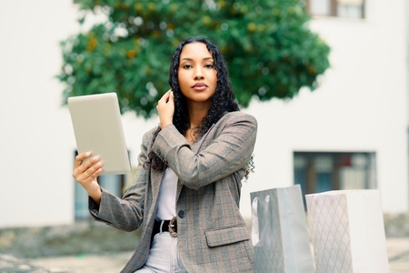 A Stylish Young Woman Engaging Enthusiastically with a Tablet Amidst Shopping Bags Around Her A Stylish Young Woman Engaging Enthusiastically with a Tablet Amidst Shopping Bags Around Her