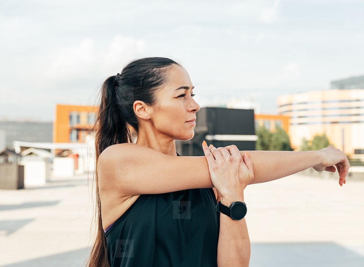 Young slim sportswoman stretching her hand before a workout on the roof