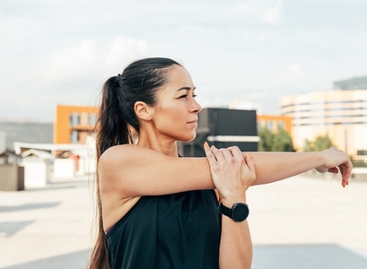 Young slim sportswoman stretching her hand before a workout on the roof