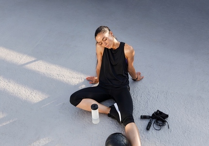 Young slim female relaxing on the roof after intense workout  Tired woman in black fitness attire relaxing with closed eyes