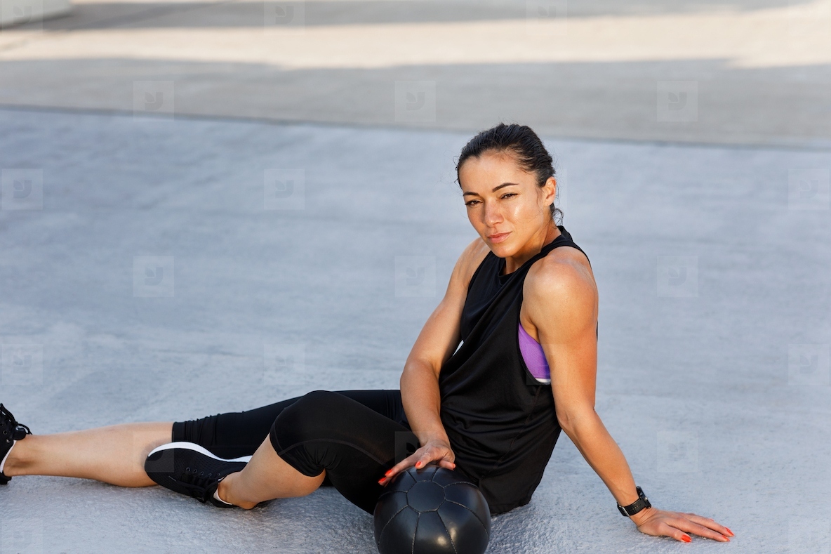 Young sportswoman relaxing on the roof during workout  Female in sportswear sitting on the roof with medicine ball