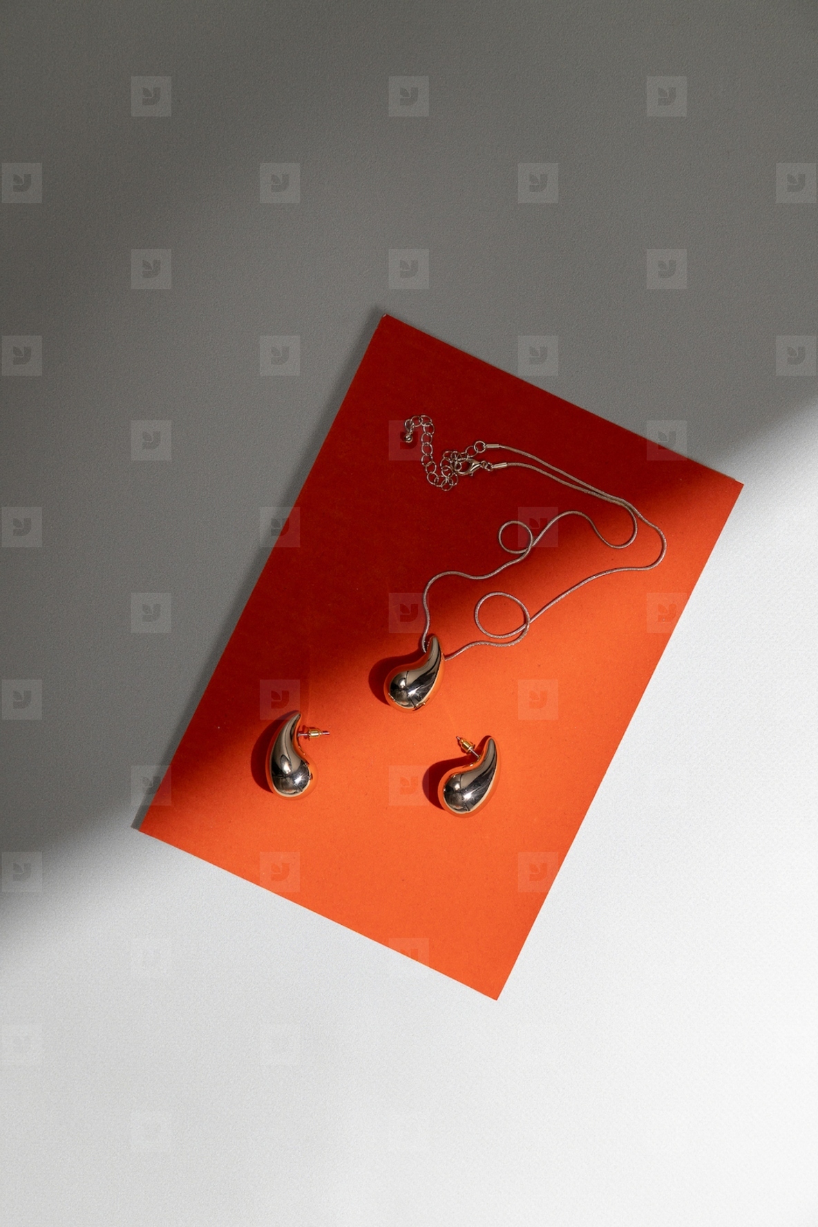Elegant golden jewelry set with pendant and earrings on orange background in minimal modern composition with shadow and light