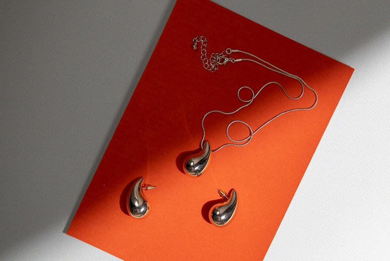 Elegant golden jewelry set with pendant and earrings on orange background in minimal modern composition with shadow and light.