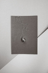 Elegant silver pendant necklace on gray paper background minimal jewelry composition with modern design and soft lighting Elegant silver pendant necklace on gray paper background minimal jewelry composition with modern design and soft lighting