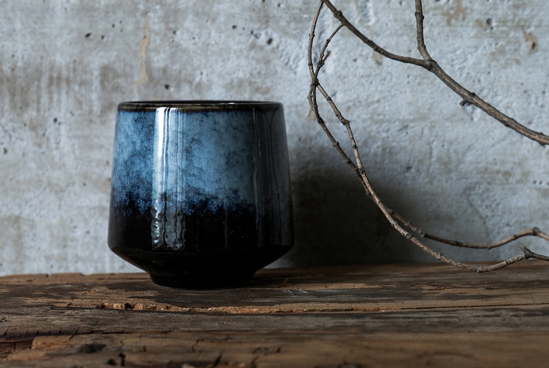 Dark ceramic cup on rustic wood with dry branch against concrete wall, minimal wabi sabi still life with natural textures.