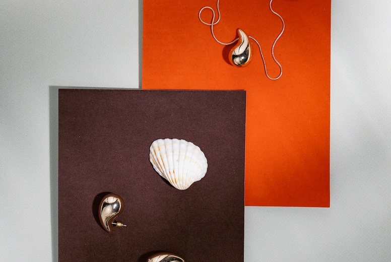 Stylish jewelry composition with golden necklace, earrings and seashell on orange and brown paper background in minimal design.