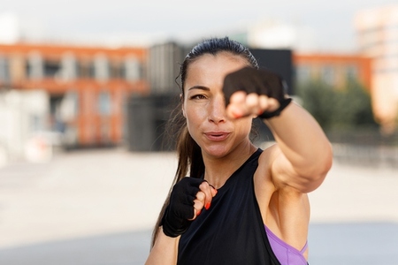 Young female practicing punches outdoors  wearing gloves  Portrait of a young woman during an intense warm up