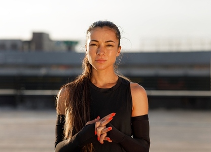 Young woman athlete wearing sportswear and arm sleeves standing outdoors and looking at camera at sunset