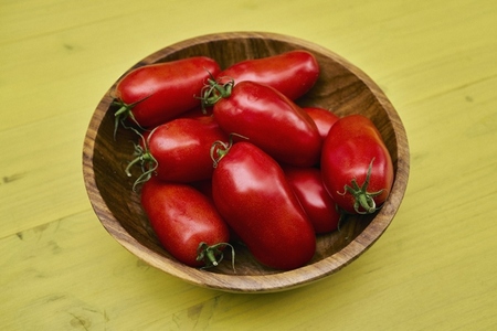 Still life of vibrant fresh red San Marzano tomatoes in wooden bowl