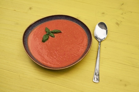 Still life of gazpacho garnished with basil in bowl next to spoon
