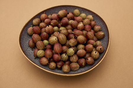 Still life of fresh ripe gooseberries in bowl against orange background