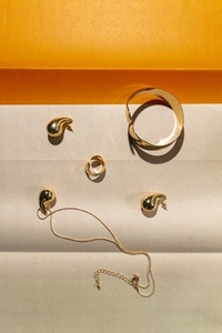 Elegant gold jewelry set with earrings bracelet and necklace on beige and orange background in minimal modern style Elegant gold jewelry set with earrings bracelet and necklace on beige and orange background in minimal modern style