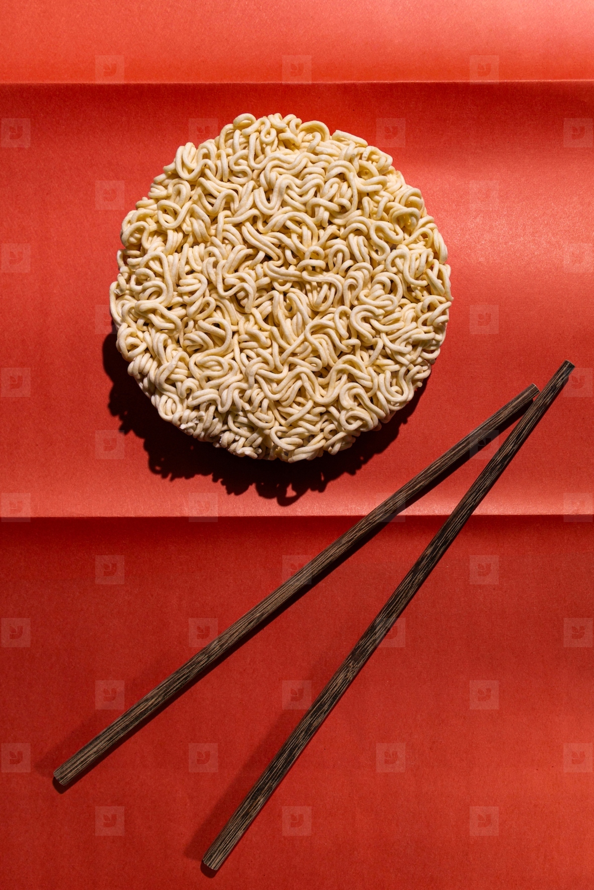 Round block of instant noodles with wooden chopsticks on red background  minimal food concept with strong contrast and shadow