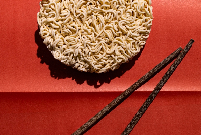 Round block of instant noodles with wooden chopsticks on red background, minimal food concept with strong contrast and shadow