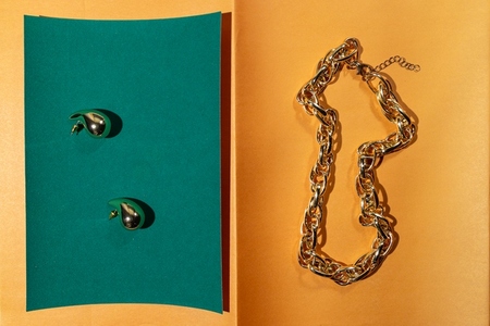 Golden chain and abstract earrings on colorful paper background modern jewelry composition with geometric light and contrast Golden chain and abstract earrings on colorful paper background modern jewelry composition with geometric light and contrast