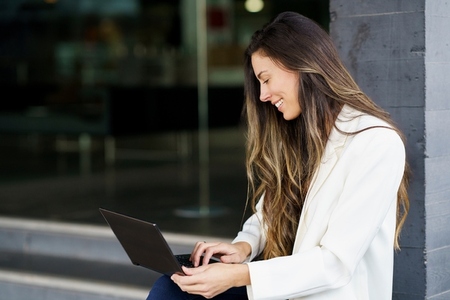 A Happy Smiling Woman Engaged with Her Laptop in a Modern Outdoor Setting  Embracing Productivity