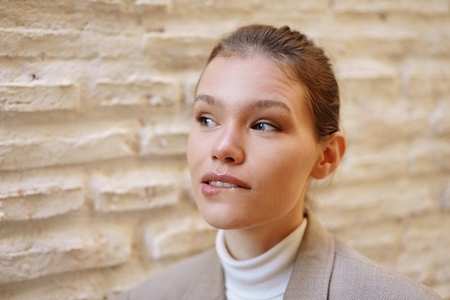 A Thoughtful Young Woman Dressed in Elegant Attire Poses Gracefully Against a Textured Wall A Thoughtful Young Woman Dressed in Elegant Attire Poses Gracefully Against a Textured Wall