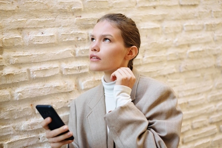 A Thoughtful Young Woman Engaged Indirectly with Her Smartphone Against a Textured Wall